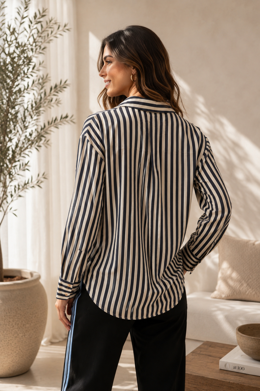 A woman shown from the back wearing a long-sleeve button-up shirt with vertical navy and cream stripes, paired with black pants, in a brightly lit, modern indoor setting.