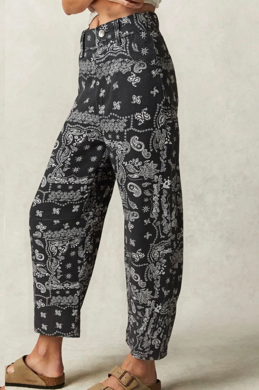 Black and white paisley print wide-leg cropped pants worn by a model, paired with tan slide sandals against a neutral textured background.