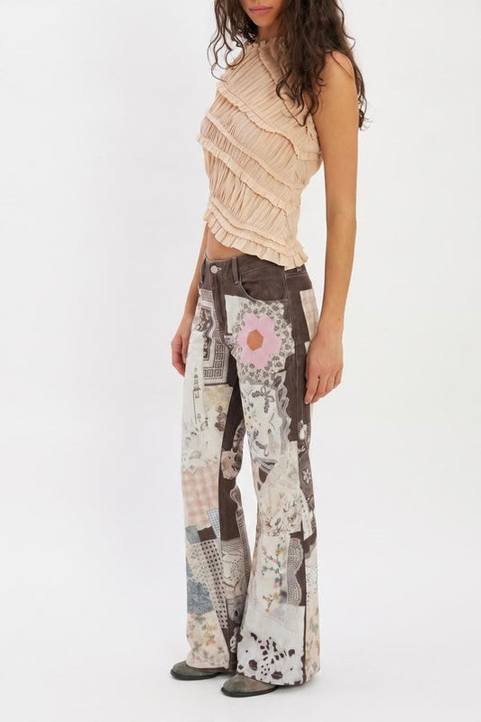 A woman wearing the Parise Patch Jean in a patchwork print with a flare silhouette, styled with a blush ruffle sleeveless top, photographed against a white studio background.