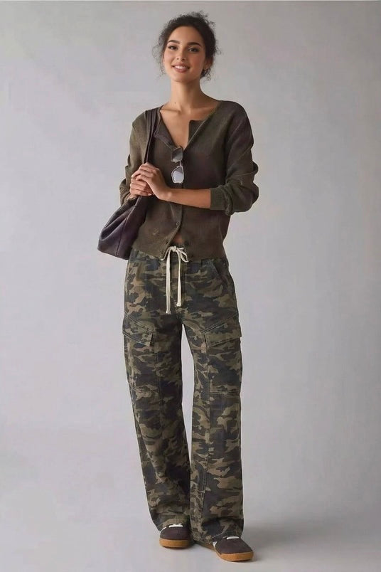A woman modeling a dark olive green cropped cardigan and camouflage print drawstring sweatpants against a neutral gray studio background.
