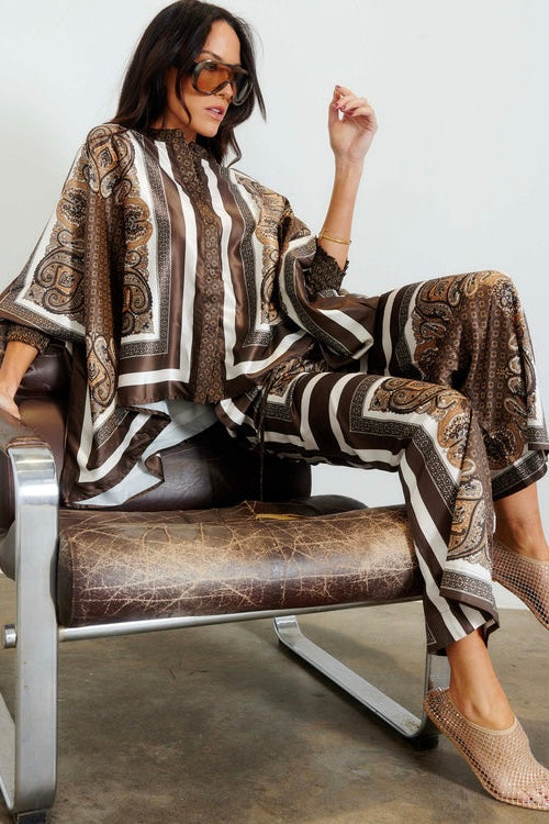 Taormina Scarf Pant — model seated on chrome leather chair wearing full co-ord in chocolate paisley scarf print with brown fishnet mule heels and sunglasses