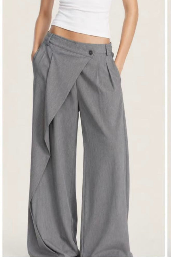 A person wearing wide-leg gray draped trousers with a white cropped top, shown from the waist down against a plain light beige studio background.