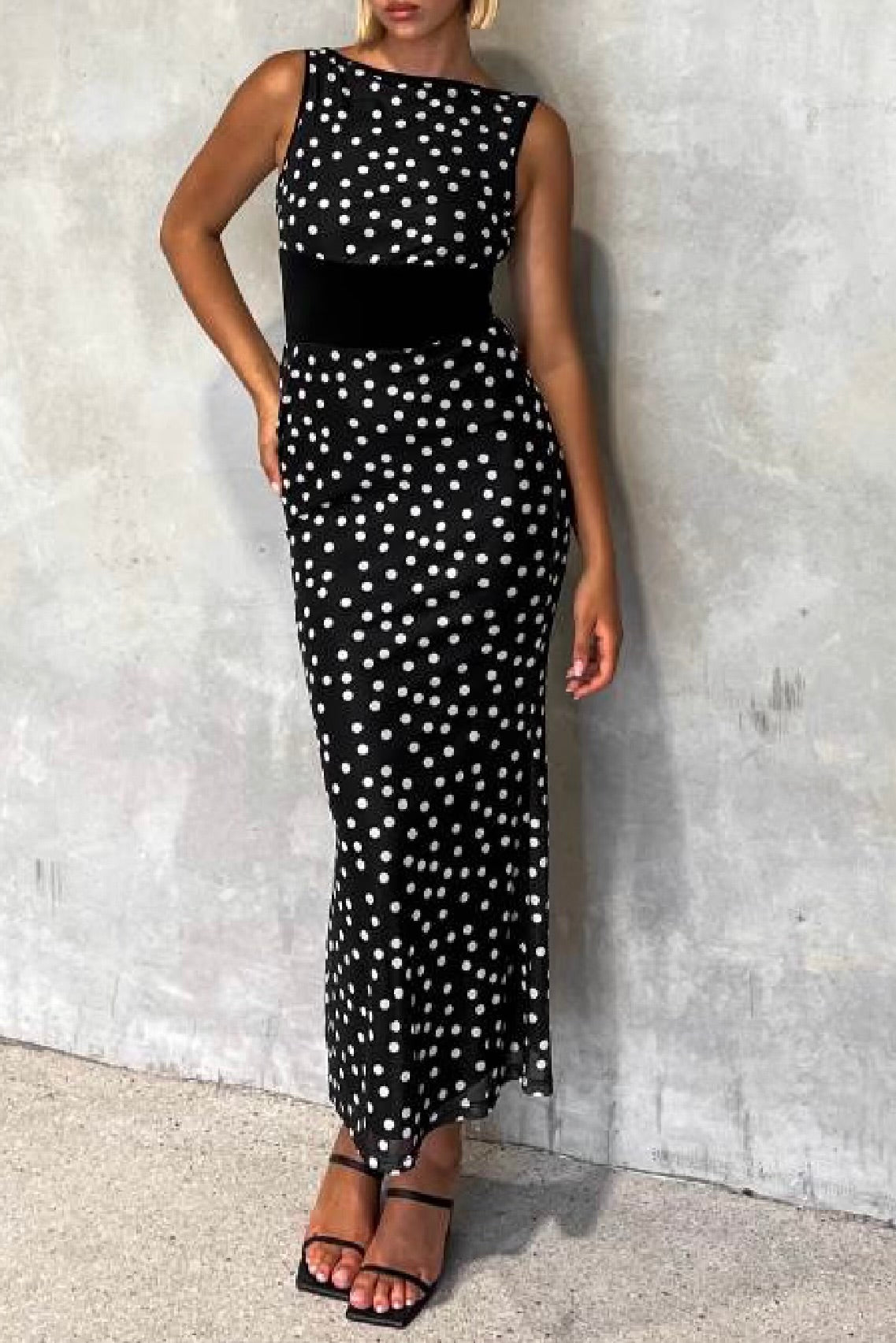 Woman wearing a black dress with white polka dots against a gray concrete wall.