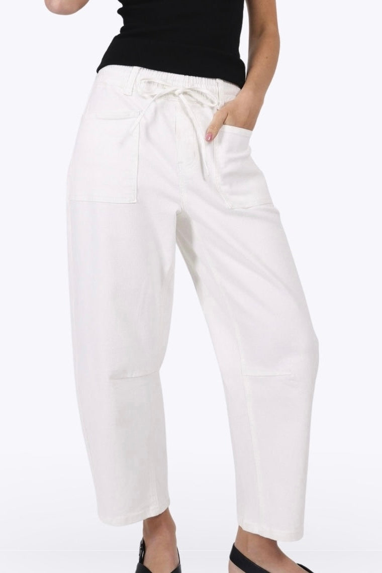 White cropped wide-leg pants with a drawstring waist and front patch pockets, shown on a model wearing a black top and black flat shoes against a plain white background.