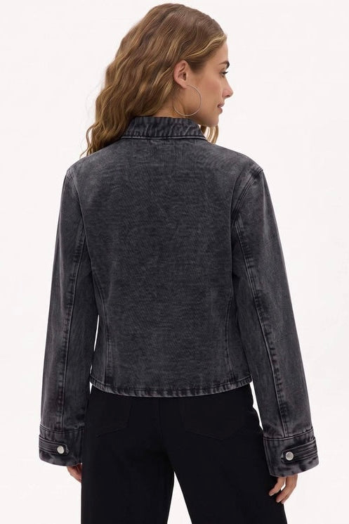 A woman shown from the back wearing a cropped dark gray washed denim jacket and black pants, photographed against a plain light background.