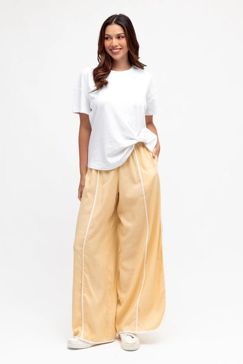 Woman wearing a white t-shirt and yellow wide leg pants on a white background