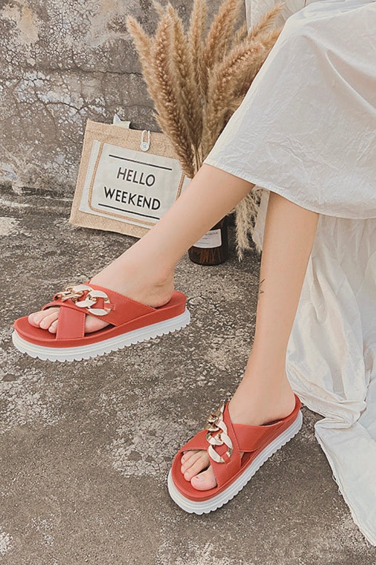 Person wearing orange sandals with decorative chain crossover  straps 