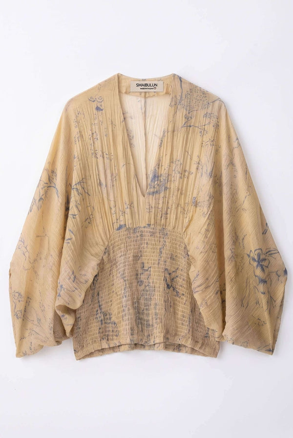 A beige long-sleeve blouse with a blue abstract print, featuring a deep V-neckline and gathered pleated detailing, shown flat against a white background.