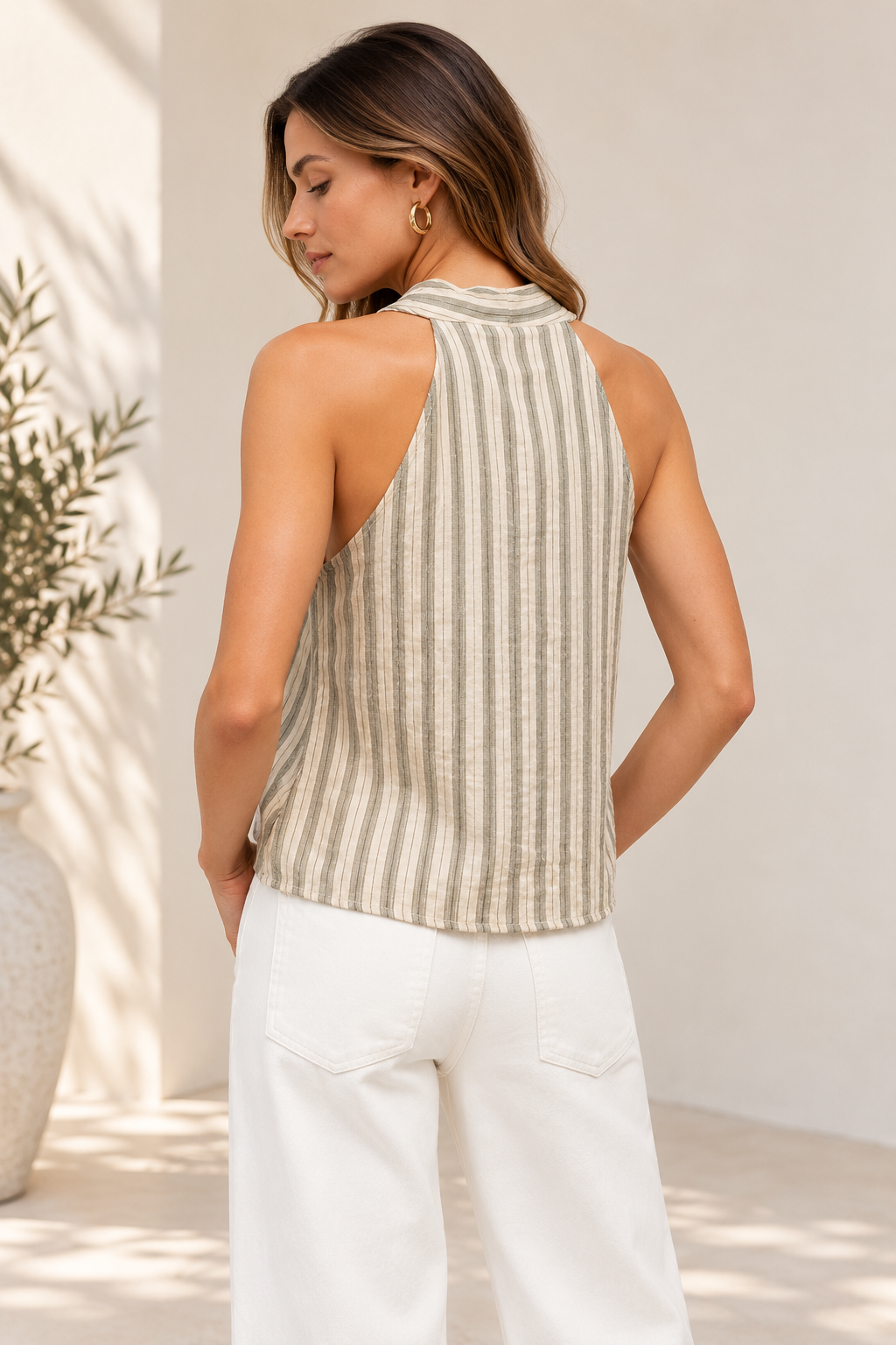 A woman shown from the back wearing a sleeveless striped knit top in beige and white, paired with white pants, in a bright, sunlit indoor setting.