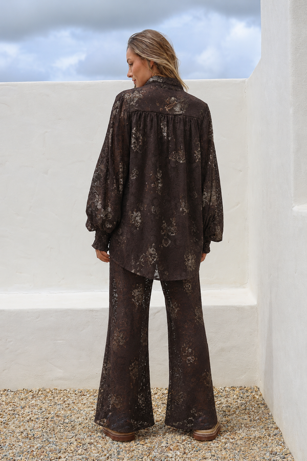 Woman wearing a dark floral outfit standing on a rooftop with a cloudy sky.