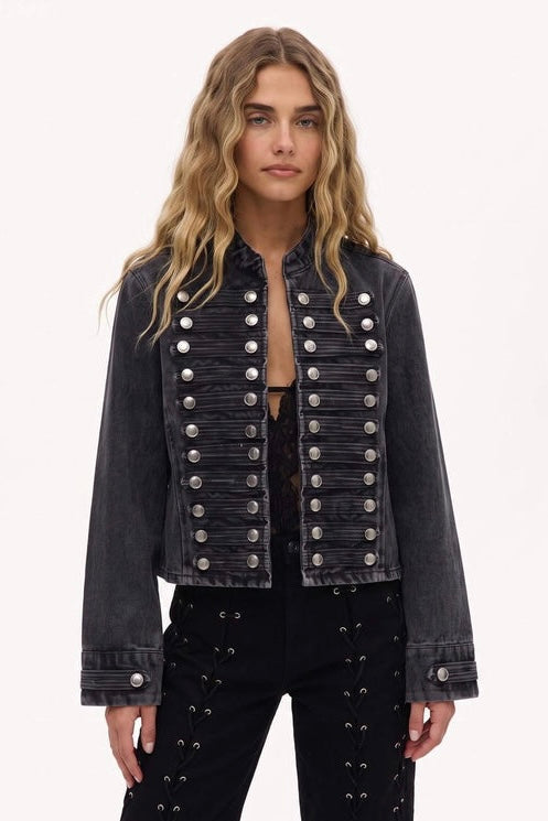 A woman modeling a dark gray cropped jacket with double-breasted silver buttons, paired with black studded pants, against a plain white background.