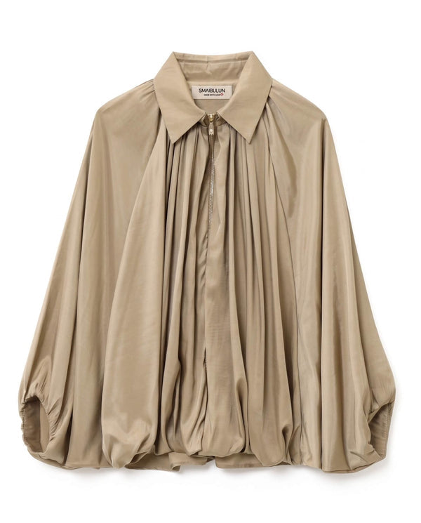 A beige long-sleeve blouse by Shablôn, featuring a pointed collar, a front button placket, and dramatic gathered pleats flowing down the front. The blouse is displayed flat against a solid white background.