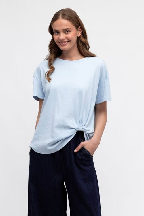 Woman wearing a light blue knot  t-shirt and dark pants 