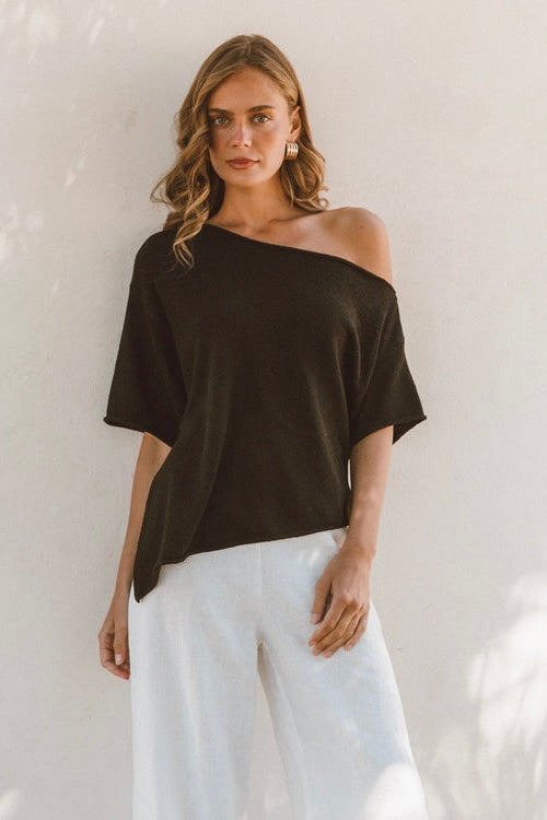 Woman wearing a black off-shoulder knit top and white pants white closet