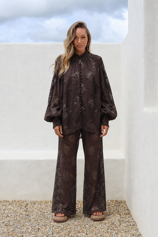 Woman wearing a dark floral outfit standing against a white wall with a blue sky.