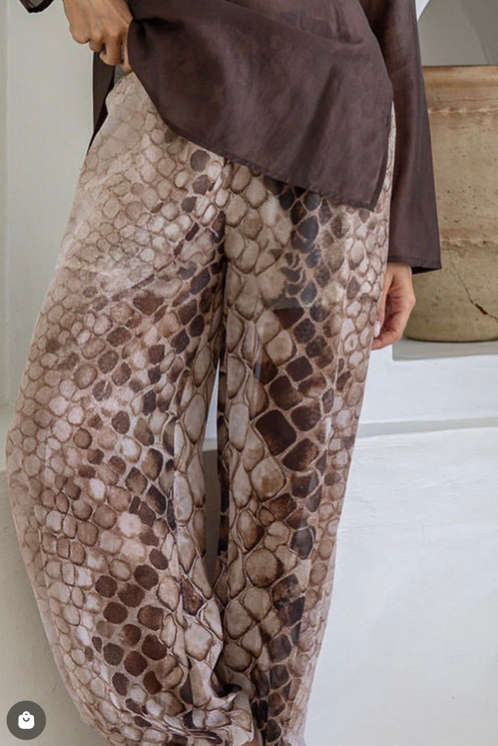 A person wearing loose, wide-leg pants with an allover snakeskin-style pattern in beige, brown, and taupe tones, paired with a dark brown top. The photo is cropped from the waist down in an indoor setting.