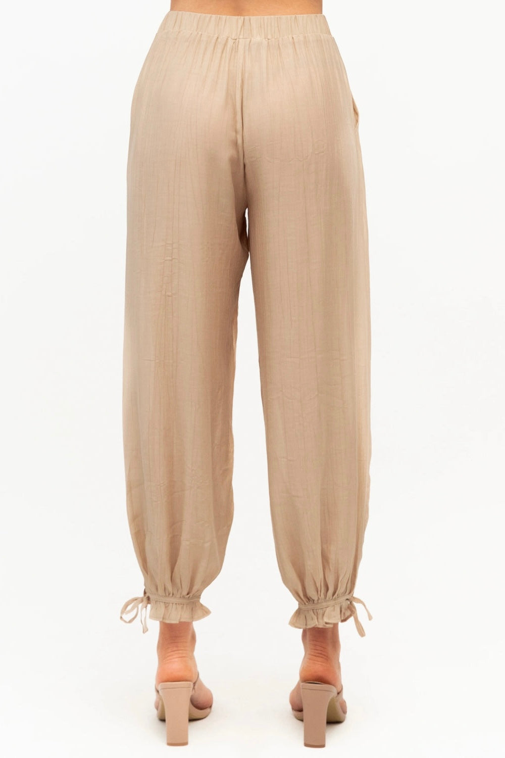 A pair of loose beige harem-style pants with elastic waistband and gathered ankle cuffs, shown on a model from the back against a plain white background.