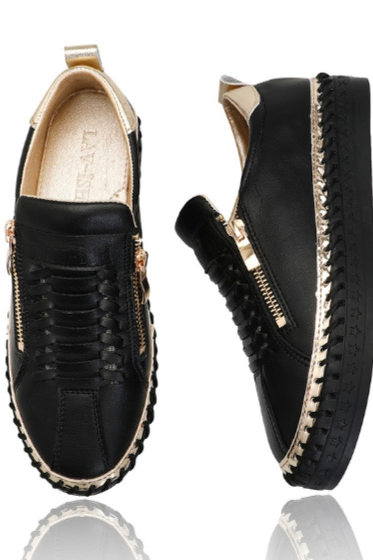 A pair of black leather platform slip-on shoes with gold-tone hardware, braided details, and a textured sole, shown from the front and side on a white background with a reflection.