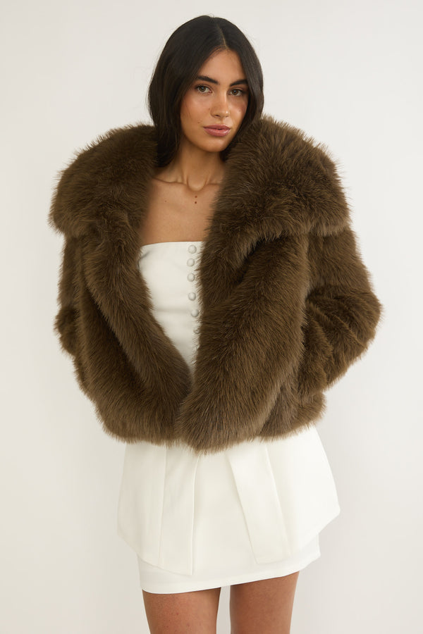 Woman wearing a brown faux fur crop coat over a white dress 