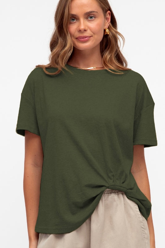Woman wearing a green t-shirt with a tuck against a plain background