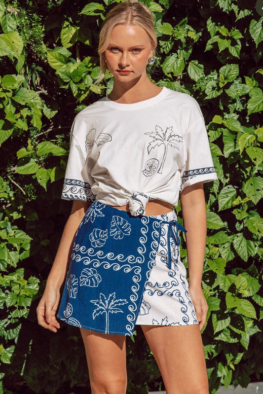 Woman wearing a white t-shirt and blue short wrap skirt with a tropical pattern 