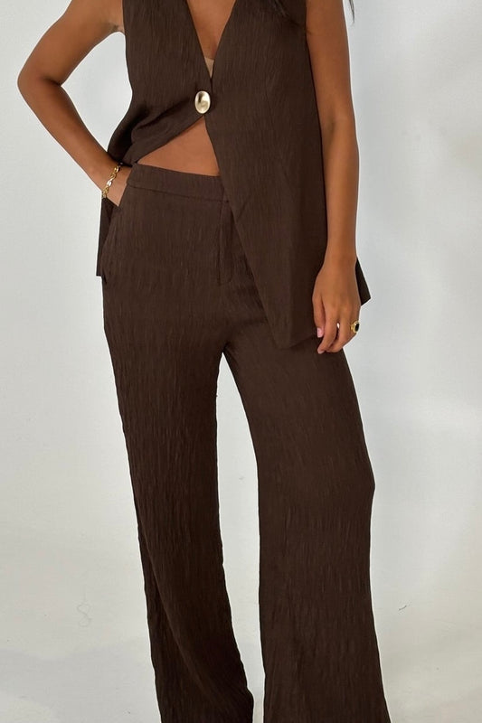 Brown outfit with a sleeveless longline vest with gold button and wide-leg pants 