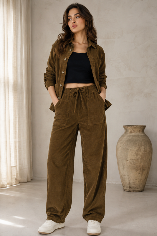 A woman modeling a pair of high-waisted, wide-leg brown corduroy pants with a drawstring waist, paired with a black crop top and white sneakers, against a plain light gray background.