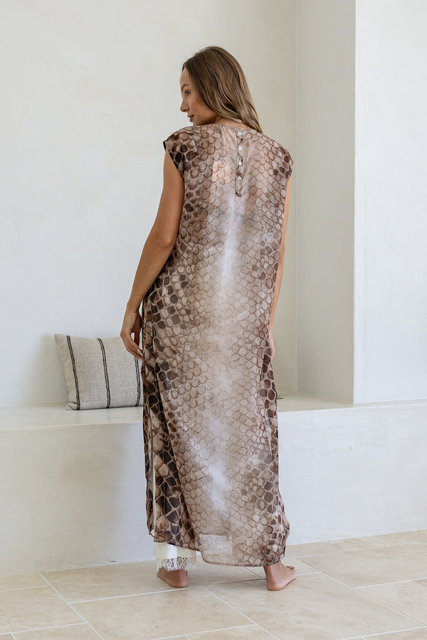 Woman wearing a long, patterned dress standing in a minimalistic room.