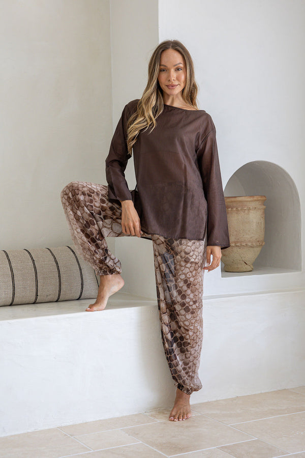 Woman wearing a brown top and patterned pants sitting on a white ledge.