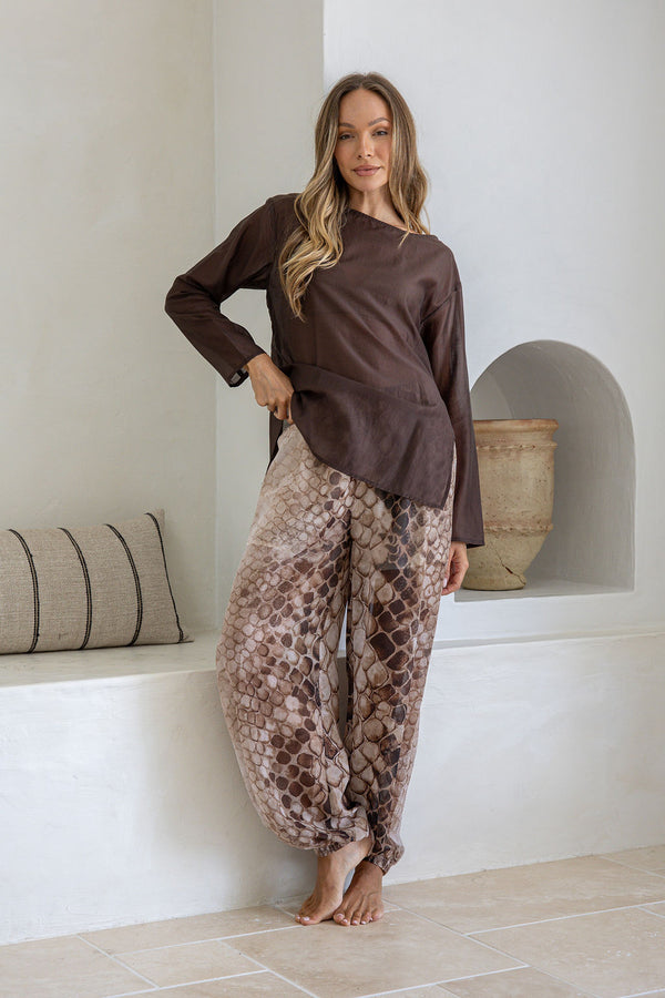 Woman wearing a brown top and patterned pants standing in a minimalistic room.