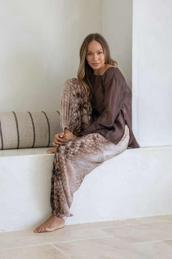 Woman sitting on a white bench wearing a brown and beige patterned dress.