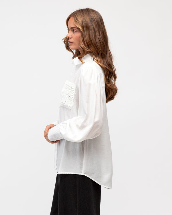 Woman wearing a white blouse with lace details on a plain background